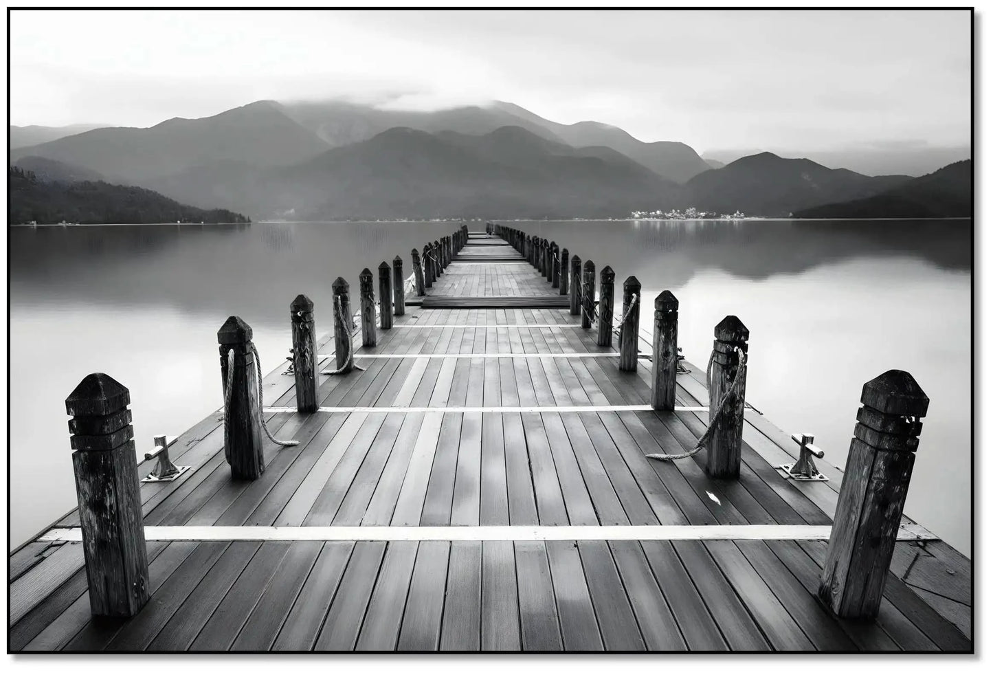 Pont en bois noir et blanc s'étendant vers l'horizon, entouré de montagnes, créant une ambiance sereine et contemplative.