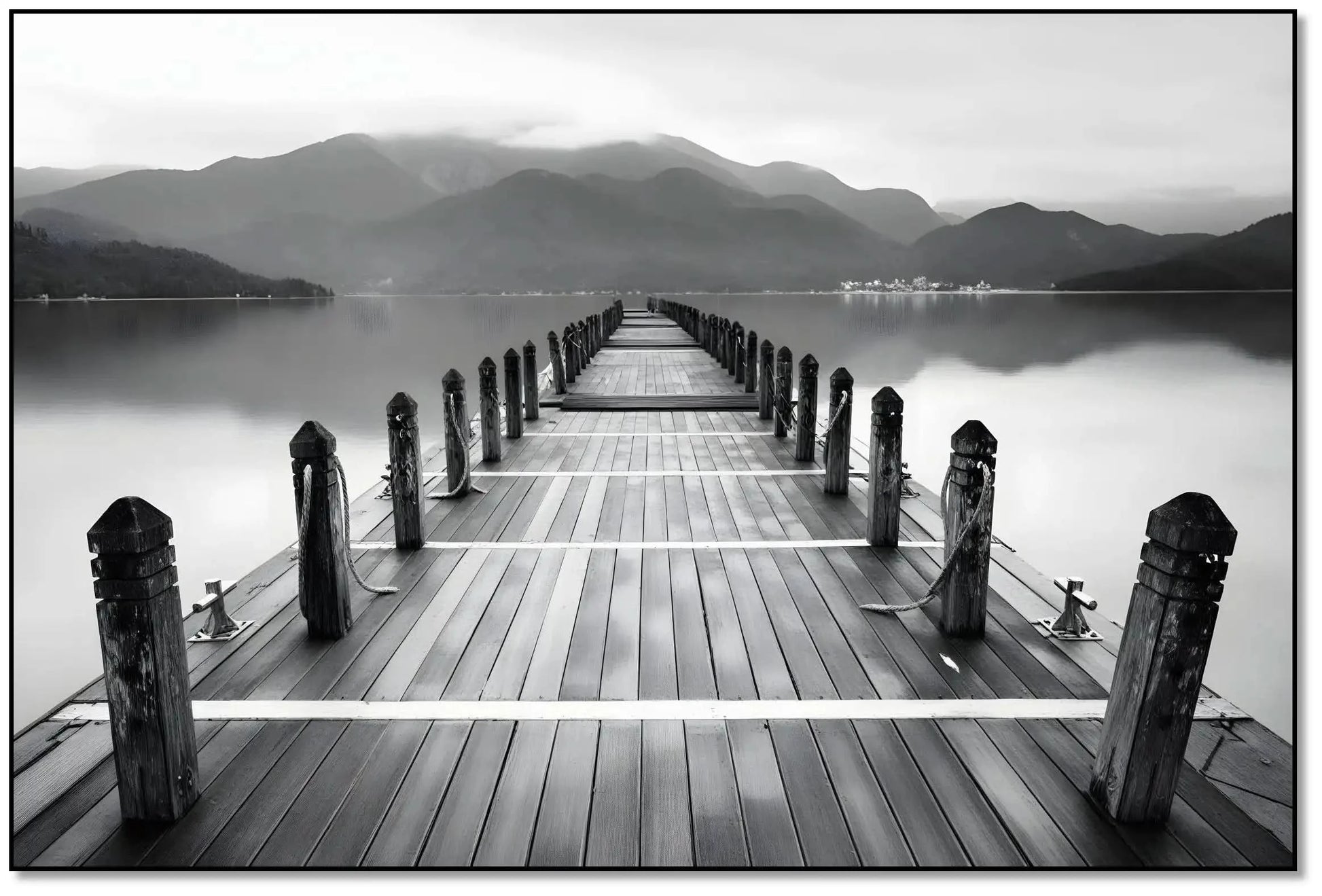 Pont en bois noir et blanc s'étendant vers l'horizon, entouré de montagnes, créant une ambiance sereine et contemplative.