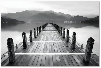 Pont en bois noir et blanc s'étendant vers l'horizon, entouré de montagnes, créant une ambiance sereine et contemplative.