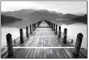 Pont en bois noir et blanc s'étendant vers l'horizon, entouré de montagnes, créant une ambiance sereine et contemplative.